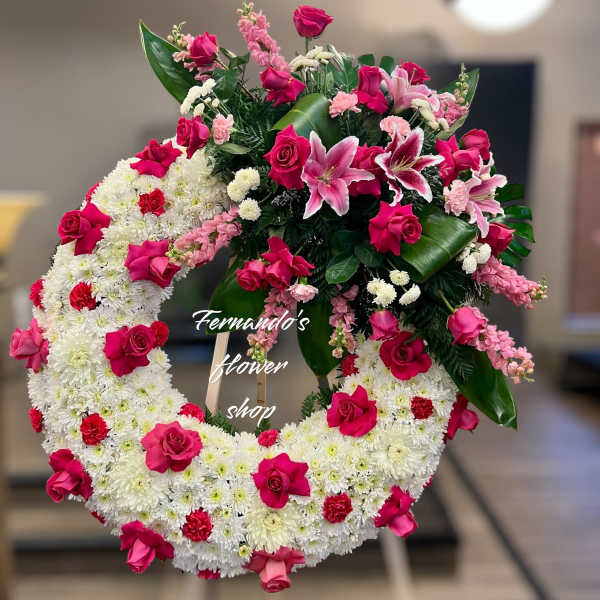Large white chrysanthemum wreath with hot pink roses and lilies on a wooden easel
