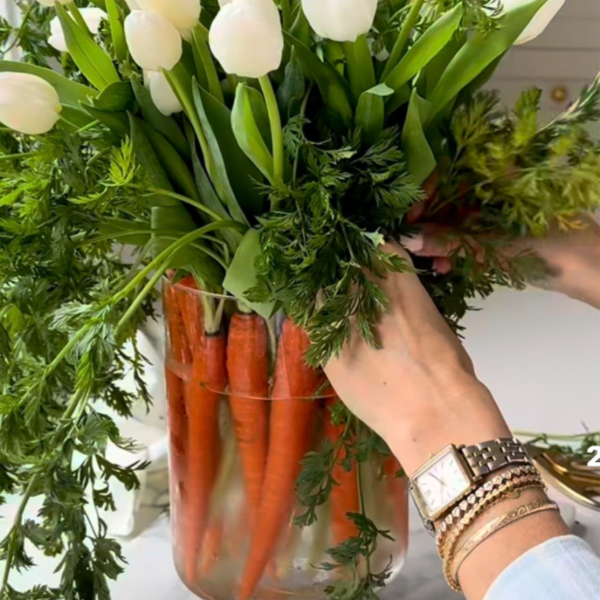 Arrangement of white tulips with carrot tops in a clear glass vase lined with whole carrots.