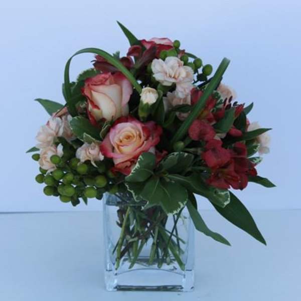 Short bouquet of red and blush roses with accent blooms in a clear square glass vase