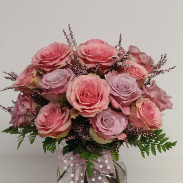 Vase arrangement of pink and lavender roses with filler blooms and a polka dot ribbon.