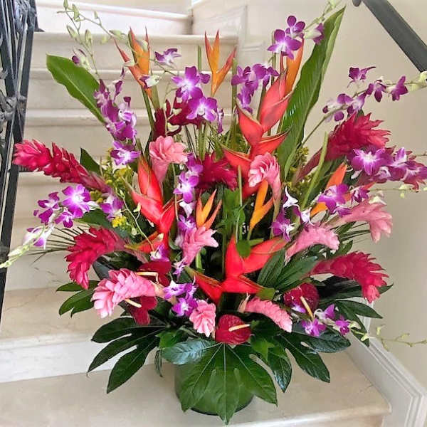 Tall tropical arrangement with pink gingers, orange heliconias, and purple orchids in a green pot
