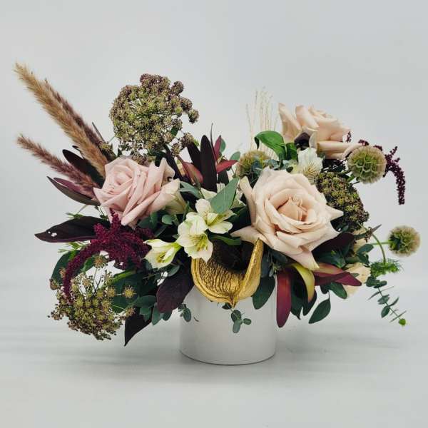 Low arrangement of blush roses, white blooms and textured accents in a white cylinder vase