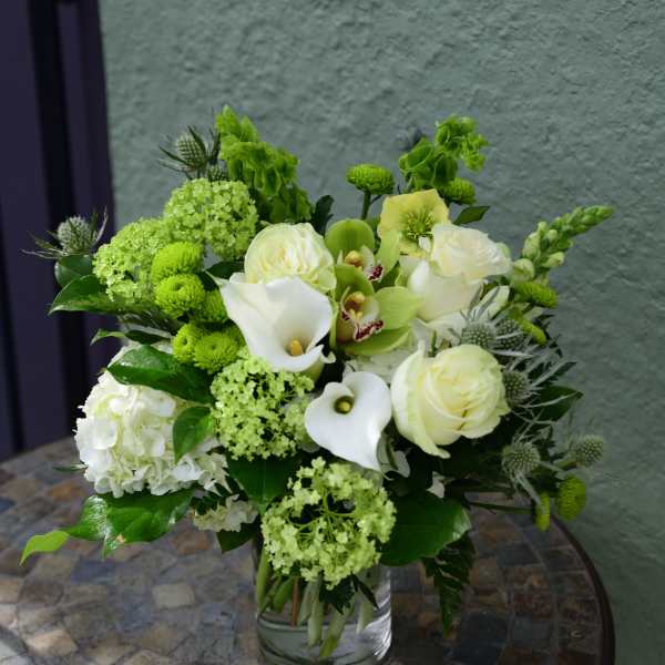 Arrangement of white roses, hydrangea, green orchids and calla lilies in a glass vase