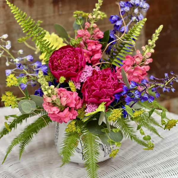 Low arrangement of bright pink and blue flowers with ferns in a white patterned ceramic container