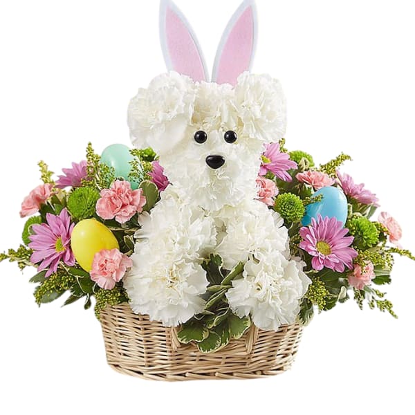 Basket arrangement with a white carnation puppy with bunny ears and pastel flowers and eggs.