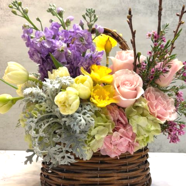Spring basket arrangement with pink roses, yellow daffodils, white tulips, hydrangeas and lavender stock