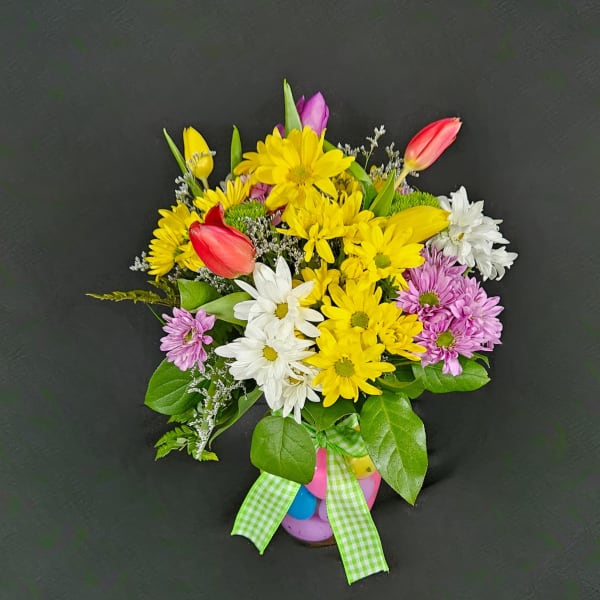 Bright arrangement of yellow daisies and multicolor tulips in a vase with pastel eggs and a green checked bow