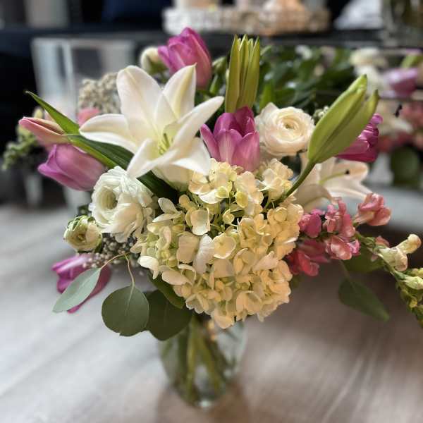 Mixed bouquet of white lilies, hydrangeas, and pink tulips in a clear glass vase
