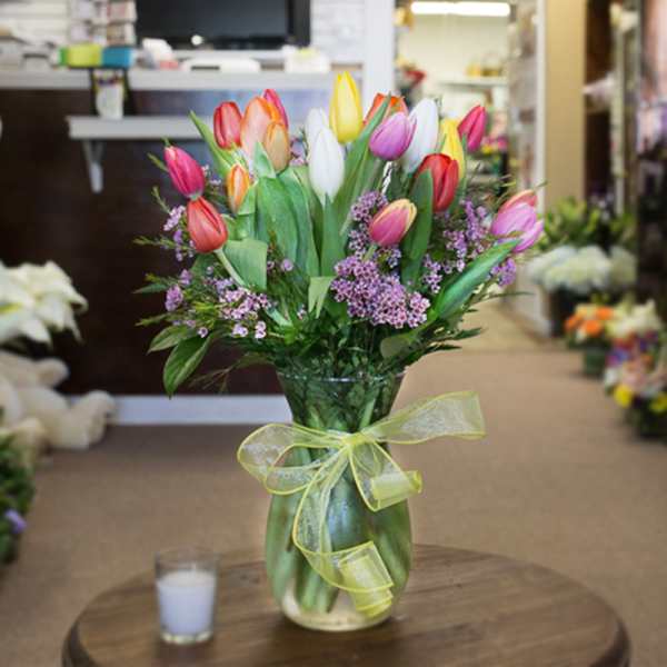 Mixed tulip bouquet with purple filler flowers in a glass vase tied with yellow ribbon