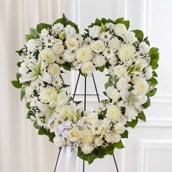 Heart-shaped white floral wreath with lilies and roses on a stand
