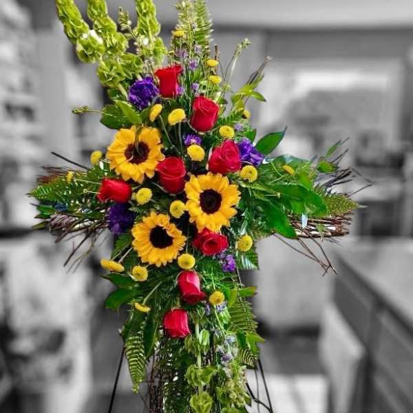 Tall cross-shaped standing spray with sunflowers, red roses, and yellow accents on an easel.