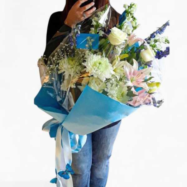 Large bouquet of white and pink flowers with blue wrapping held by a person in jeans
