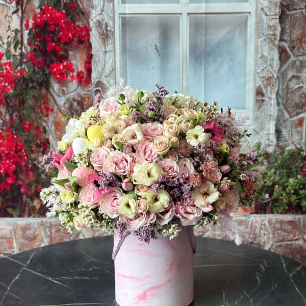 Lush pastel pink and cream flower arrangement in a pink marbled hat box on a dark table