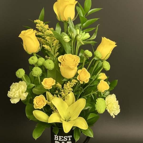 Tall yellow rose and lily arrangement in a black 'Best Dad Ever' mug on a wood slice base