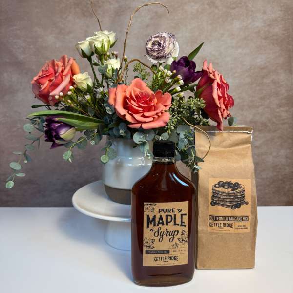 Coral and white floral arrangement in a white vase with maple syrup bottle and pancake mix bag