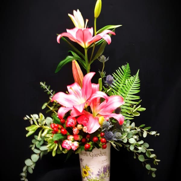 Tall arrangement of pink lilies, small roses, and red berries in a decorative herb garden vase