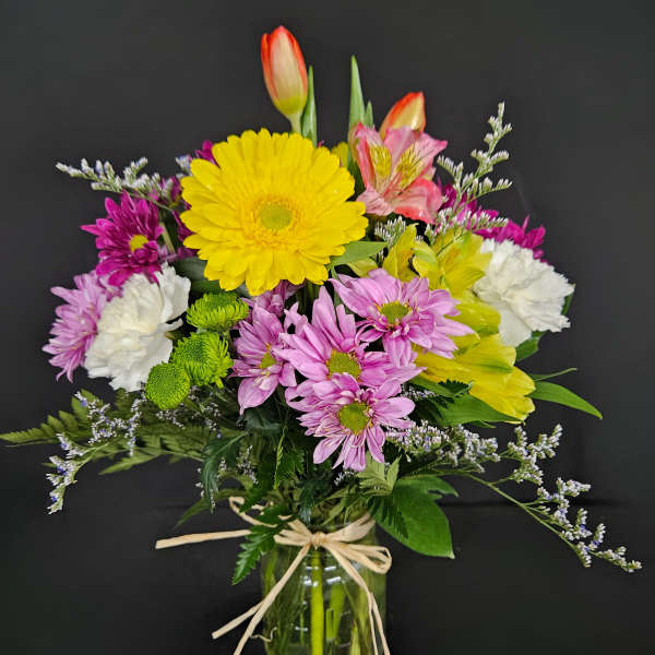 Mixed spring bouquet with yellow gerbera, tulips, carnations and daisies in a glass jar vase.