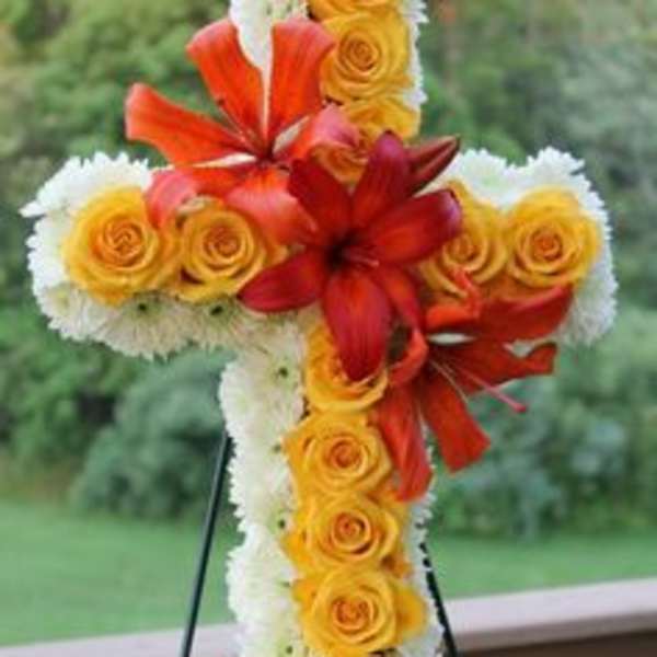 Standing cross-shaped floral spray with yellow roses, white blooms, and orange lilies on an easel