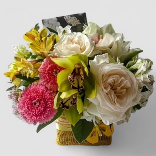 Compact arrangement of ivory roses, green orchids, pink mums and yellow alstroemeria in a square wrapped container