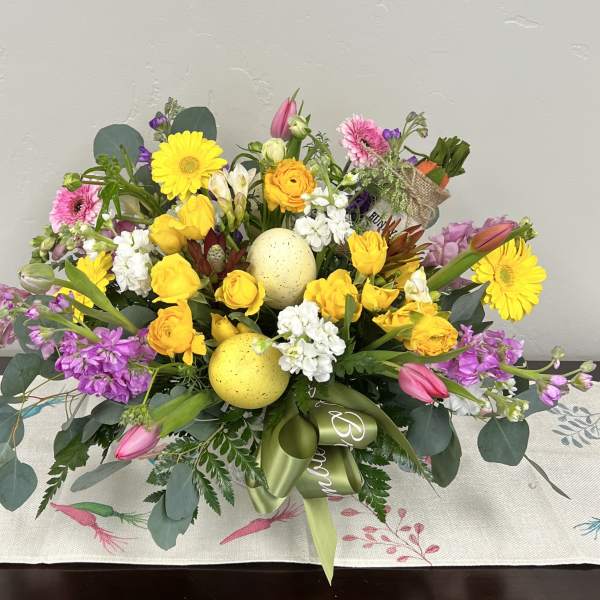 Colorful mixed spring arrangement with yellow, pink, white, and purple flowers and decorative speckled eggs.