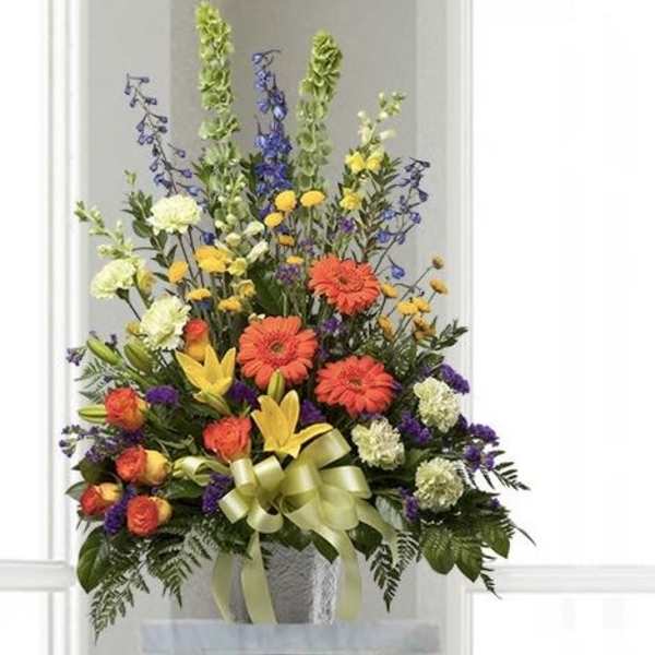 Tall mixed arrangement with orange gerberas, yellow lilies, roses, and Bells of Ireland in a white vase