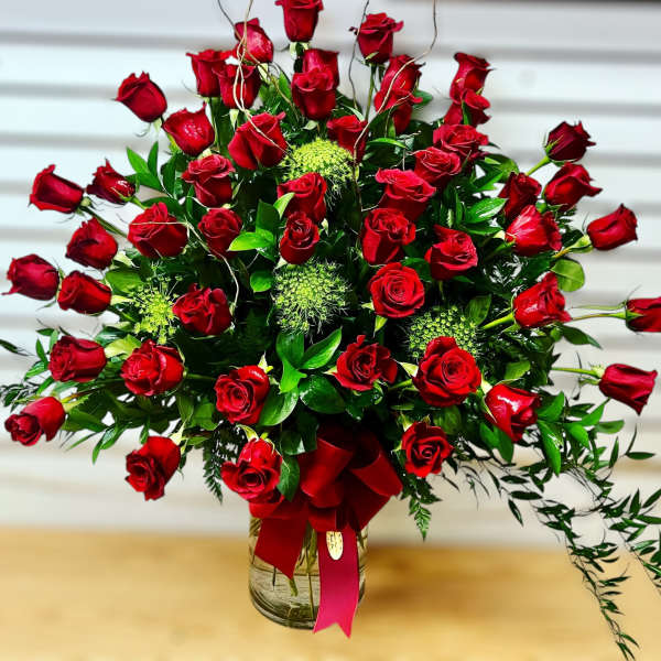 Large fan-shaped arrangement of red roses in a clear glass vase with a red bow.