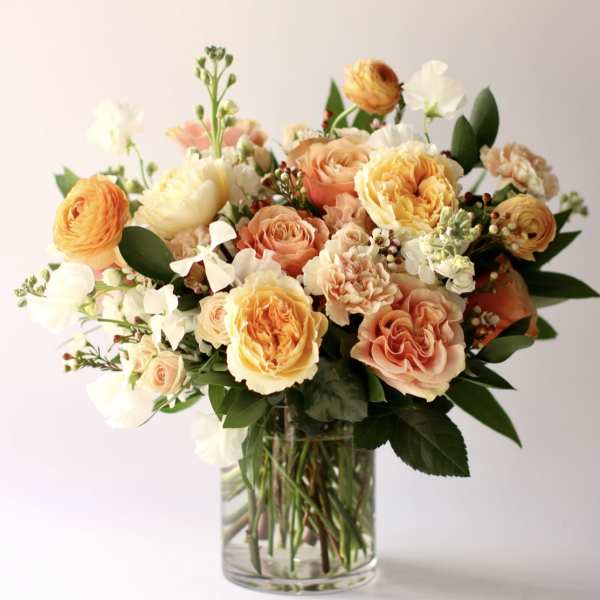 Peach and yellow rose arrangement with white accents in a clear glass vase.