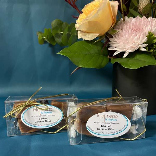 Yellow rose and pink mum arrangement beside two clear boxes of wrapped caramel candies.