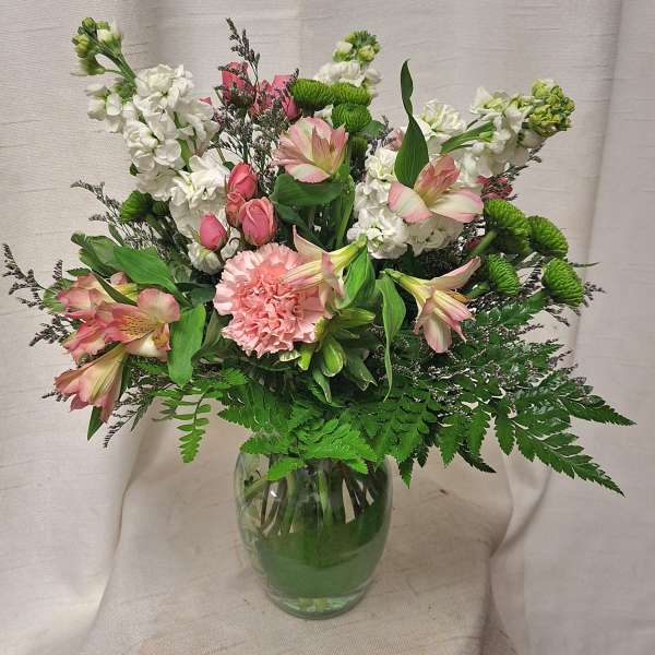 Mixed bouquet of pink and white flowers with green accents in a clear glass vase