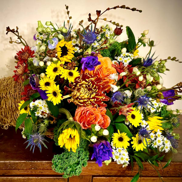 Colorful fall cornucopia arrangement with yellow sunflowers, orange roses, and mixed blooms in a woven horn basket