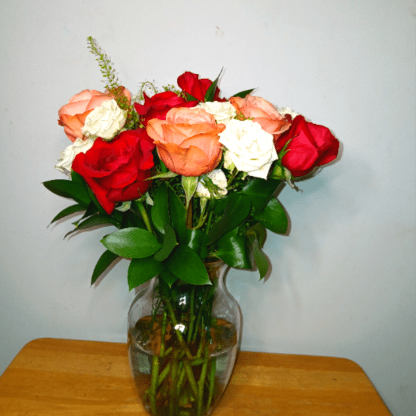 Mixed red, peach, and white roses arranged in a clear glass vase on a wooden surface.