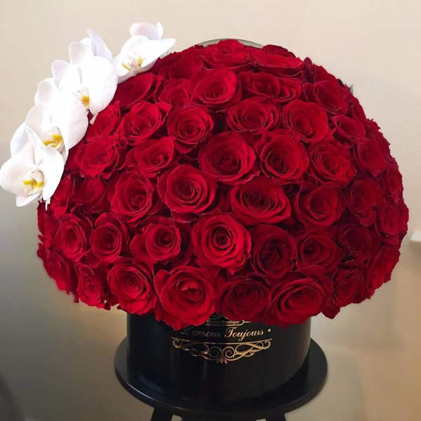 Round hatbox of densely packed red roses with a side accent of white orchids in a black container.
