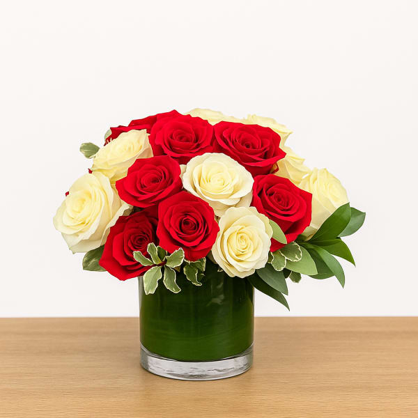 Red and cream roses arranged tightly in a short glass vase lined with green foliage.