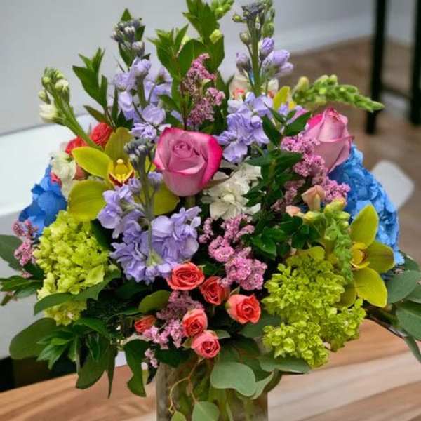 Colorful mixed bouquet with pink roses, orchids, hydrangeas and stock in a clear glass jar vase