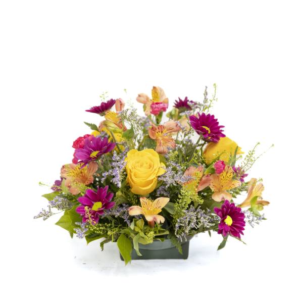 Low arrangement of yellow roses, pink daisies, and peach alstroemeria in a green rectangular container