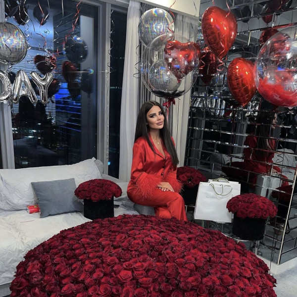 Large dome of red roses with boxed roses and heart balloons in a modern room.