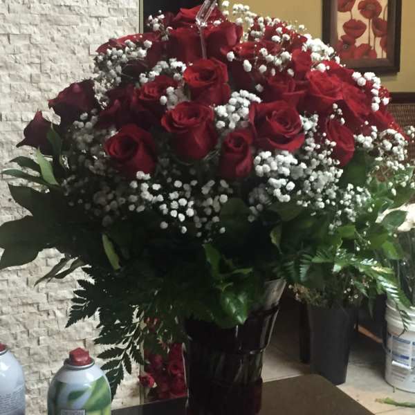 Large bouquet of red roses and white filler flowers in a tall dark glass vase