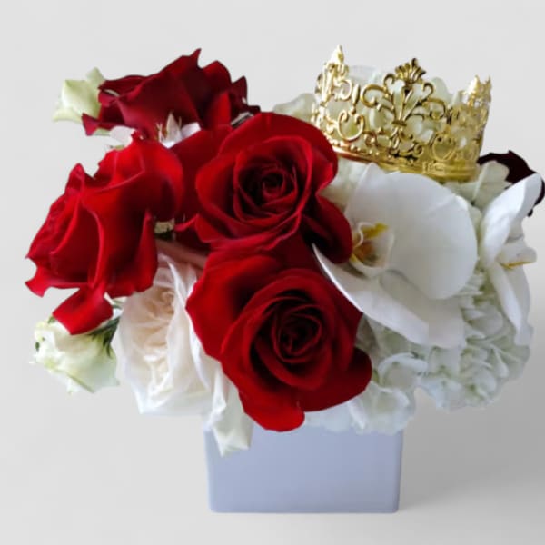 Compact arrangement of red roses and white orchids with a gold crown in a white cube vase