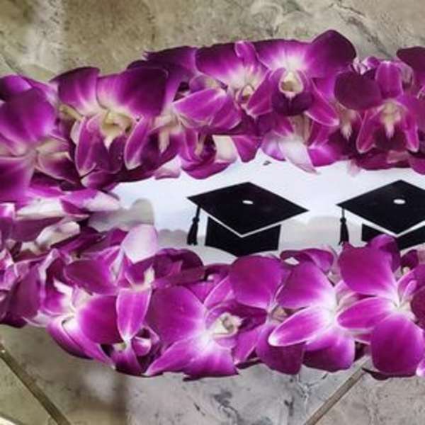 Purple orchid lei arranged around a white insert decorated with black graduation caps