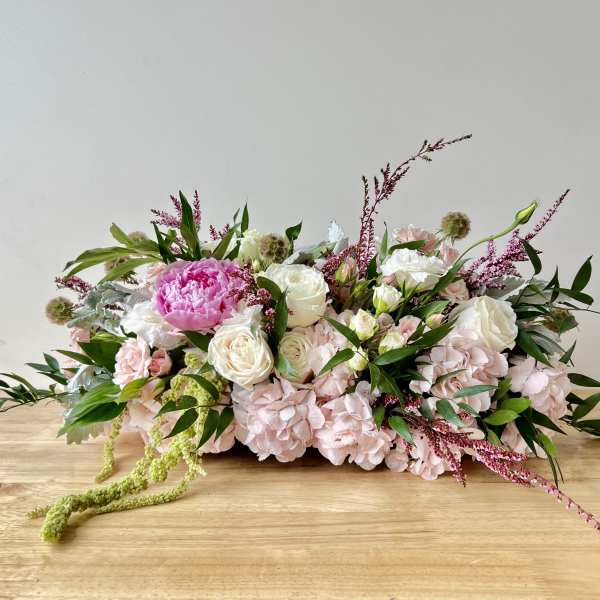 Low centerpiece of pink hydrangeas, white roses, and a bright pink peony on a wooden table