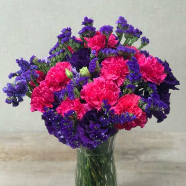 Bright pink carnations and purple flowers arranged in a clear glass vase