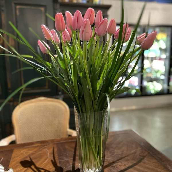 Tall arrangement of pink tulips in a clear glass vase on a wooden table