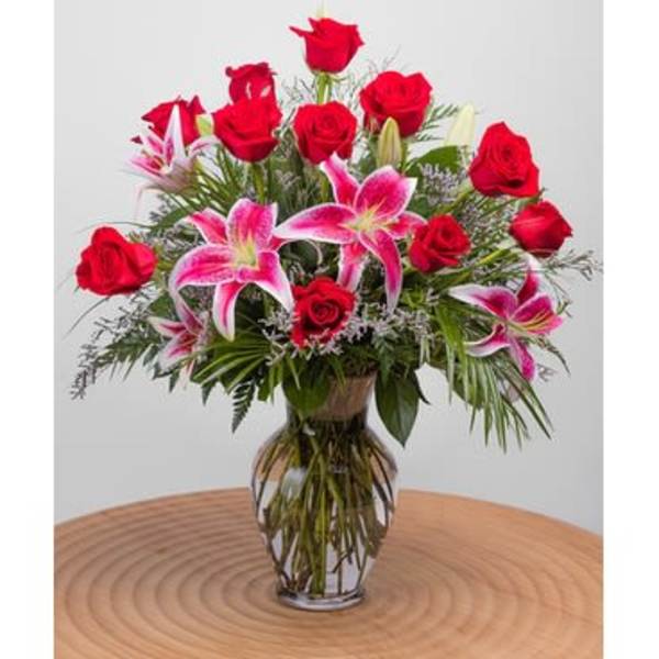 Tall arrangement of red roses and pink lilies in a clear glass vase