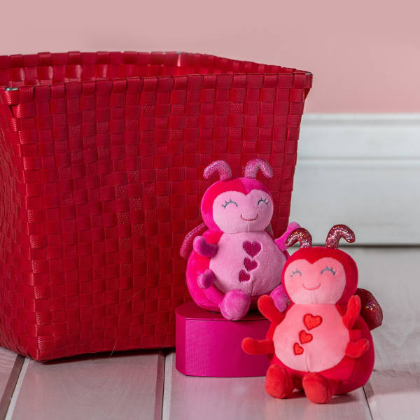 Two pink and red heart-themed plush ladybug toys beside a red woven basket