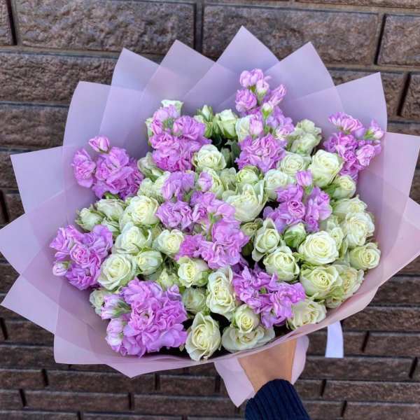 Hand-tied bouquet of cream spray roses and light lavender blooms wrapped in soft pink paper