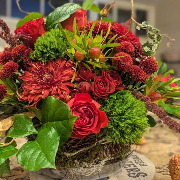 Low arrangement of red roses and mums with bright green accents in a rustic basket