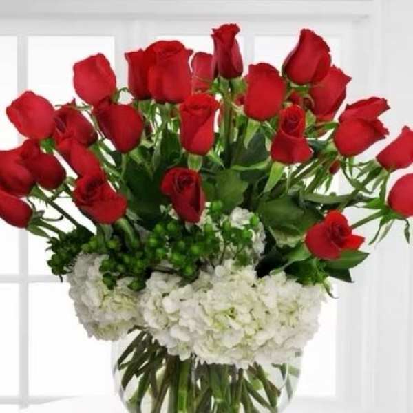 Round vase of red roses arranged above white hydrangeas in a clear glass bowl