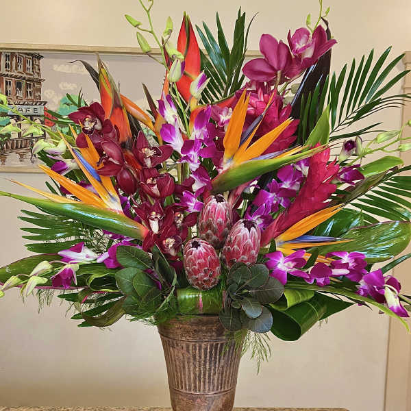 Tall tropical arrangement with orange birds of paradise, purple orchids, and protea in a bronze urn vase