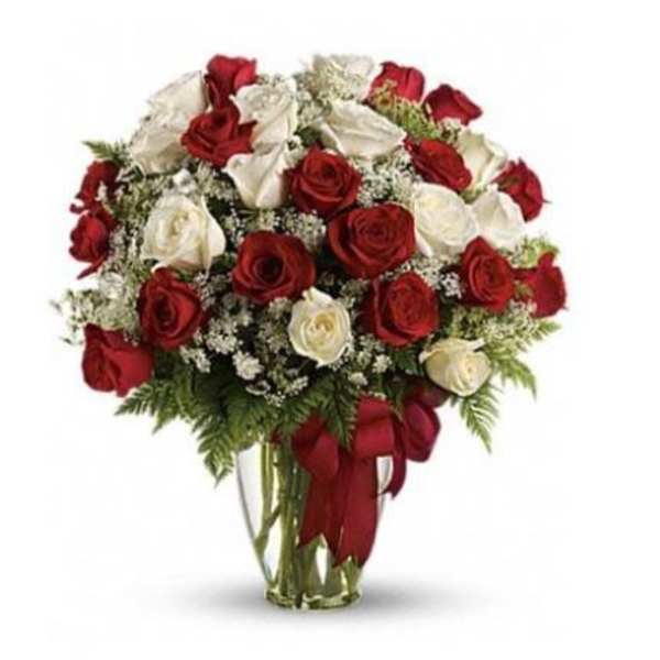 Arrangement of red and white roses with small white filler flowers in a clear glass vase with a red bow.