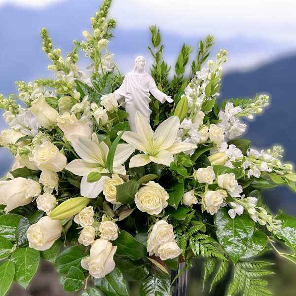 White lilies and roses arranged around a white religious figurine